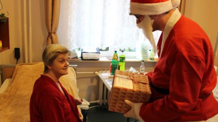 Na zdjęciu znajduje się Święty Mikołaj, który obdarowuje Mieszkankę pięknym prezentem.