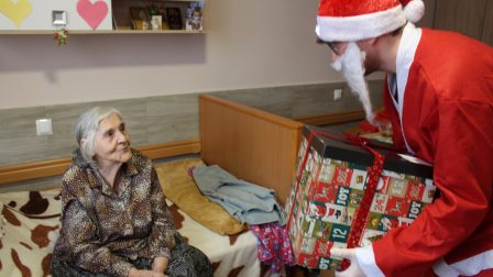 Na zdjęciu znajduje się uśmiechnięta Mieszkanka, która rozmawia i otrzymuje prezent od Świętego Mikołaja.